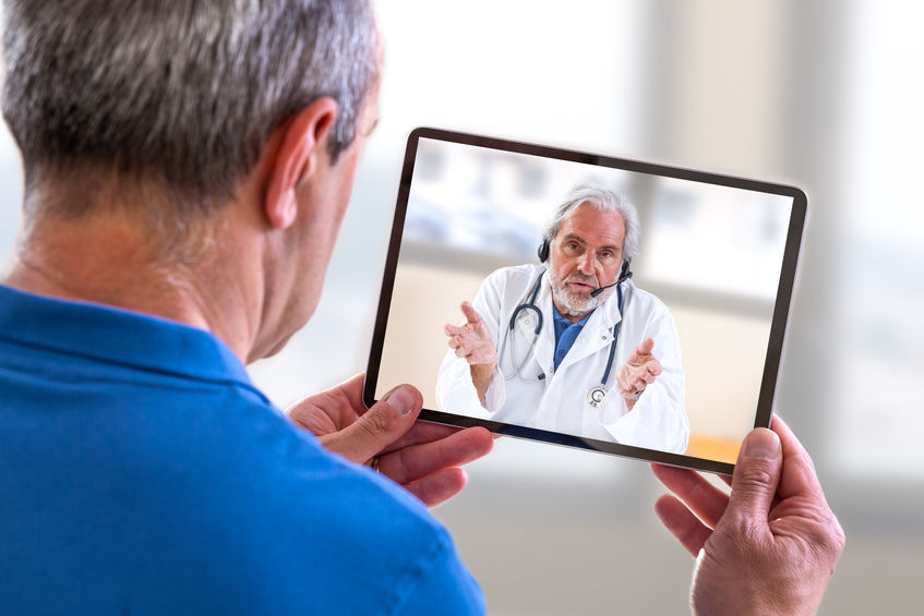 Remote consultation- Doctor sitting at hospital, with laptop, having an online call with patient showing tablet device